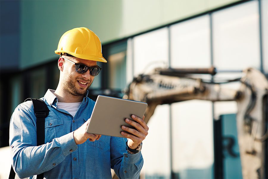 Specialized Business Insurance - Construction Engineer Wearing Hard Hat and Using a Digital Tablet at the Construction Site on a Sunny