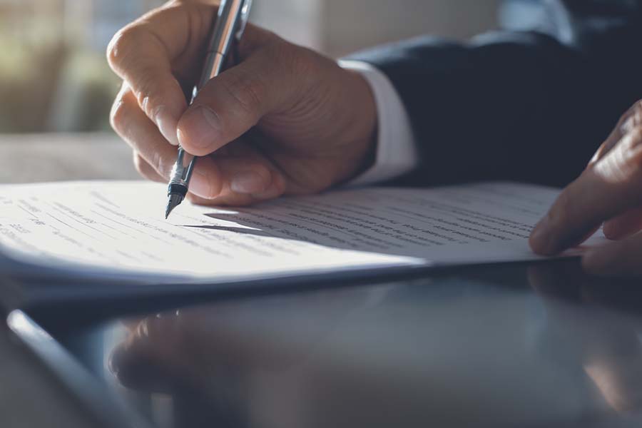 Group Captive Insurance - Closeup of a Business Owner Signing an Agreement for Captive Insurance While Sitting at His Desk